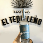 Bottle of El Tequileño tequila held in front of the distillery wall during a tasting tour in Tequila, Jalisco