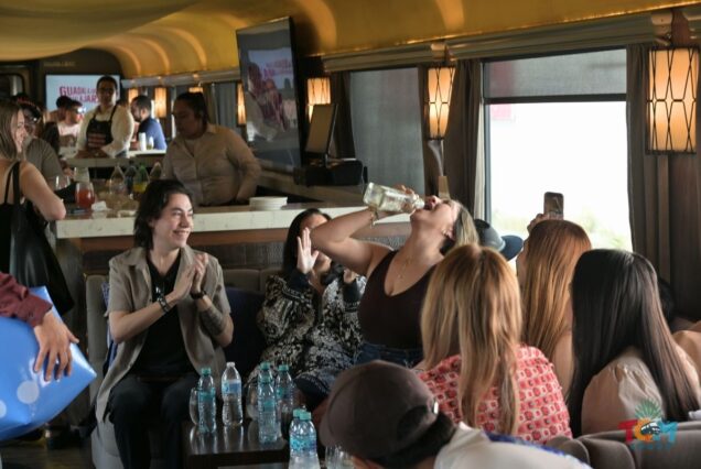 Group of passengers cheering as a woman takes a tequila shot inside the Tequila Express Train during the tequila train experience.