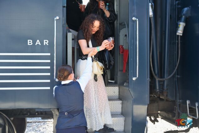 Tequila Express staff assisting a passenger stepping off the bar car while holding drinks.