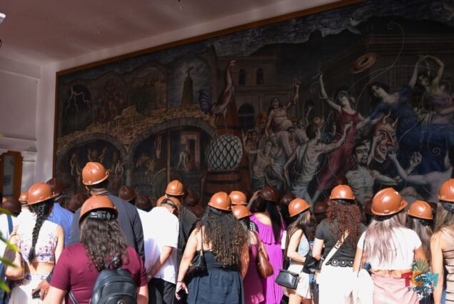 Tour group wearing brown hard hats observing a large historic mural inside Casa Sauza.