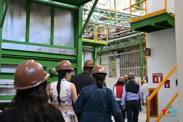 Tour group wearing hard hats walking through an industrial area inside the tequila processing plant.