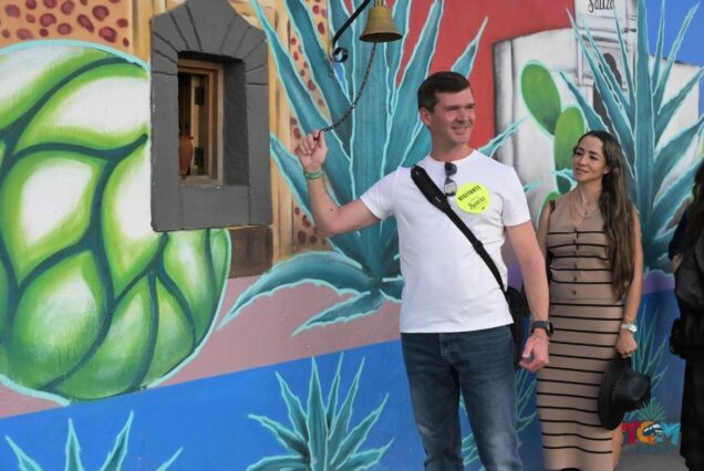Tourist ringing a small bell attached to a colorful agave mural in Tequila, Jalisco.