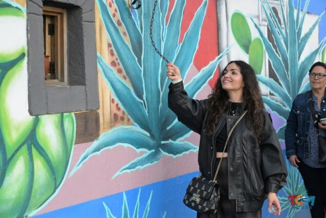 Woman ringing a bell next to an agave-themed mural during the Tequila Express Train tour.